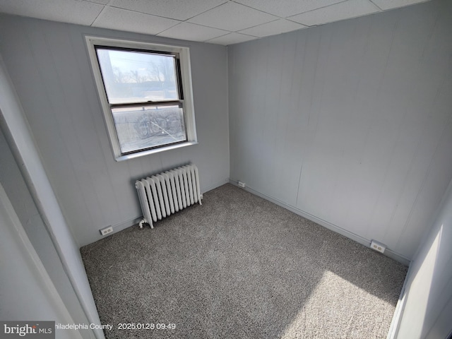 unfurnished room featuring a drop ceiling, radiator, and carpet