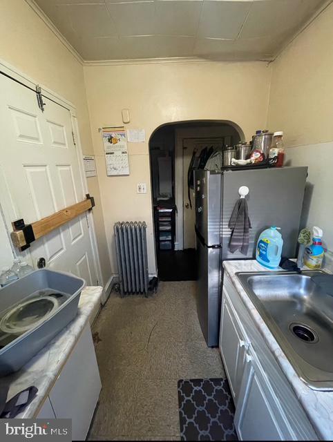 kitchen featuring white cabinetry, radiator, sink, and stainless steel fridge