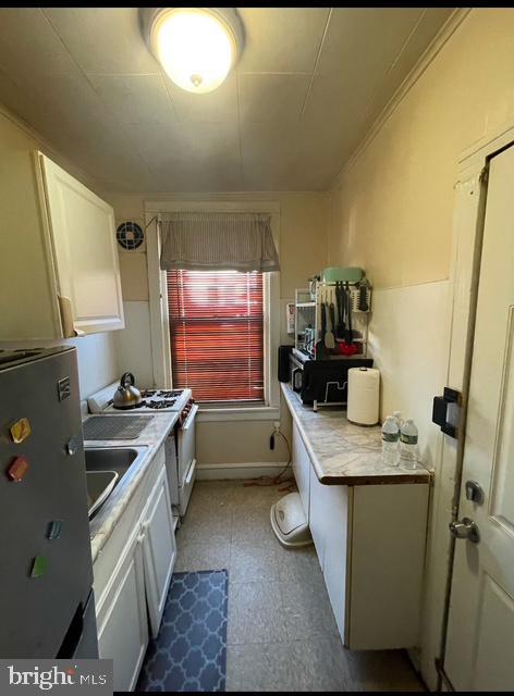 kitchen featuring stainless steel fridge, gas range oven, and white cabinets