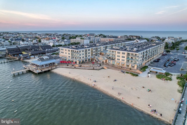 aerial view at dusk featuring a water view and a beach view