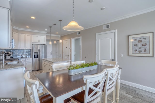 dining space featuring sink, ornamental molding, and light wood-type flooring