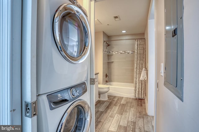 washroom with stacked washing maching and dryer, electric panel, and light wood-type flooring