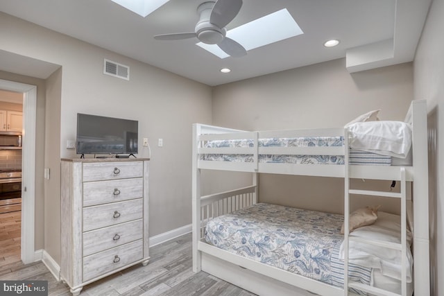 bedroom with light hardwood / wood-style flooring, ceiling fan, and a skylight