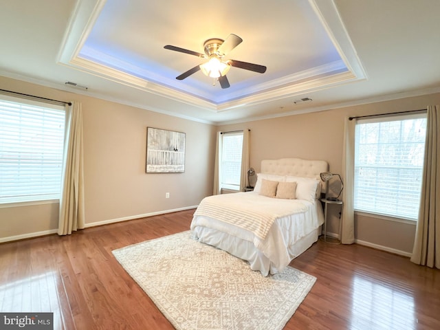 bedroom with crown molding, wood-type flooring, a raised ceiling, and multiple windows