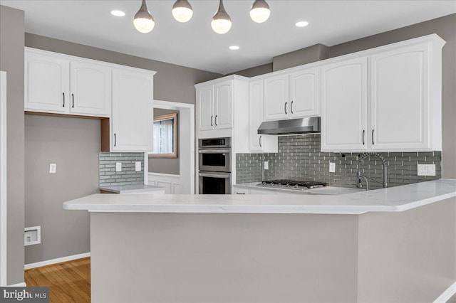 kitchen with white cabinetry, decorative light fixtures, kitchen peninsula, stainless steel appliances, and backsplash