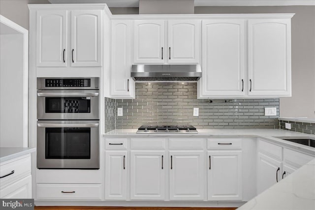 kitchen featuring backsplash, white cabinets, appliances with stainless steel finishes, and exhaust hood