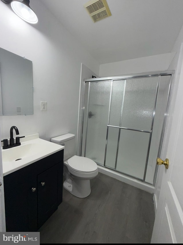 bathroom featuring wood-type flooring, toilet, vanity, and walk in shower