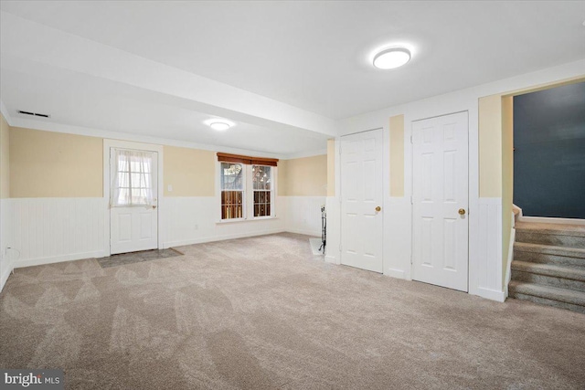 basement featuring carpet floors, a wainscoted wall, and stairs