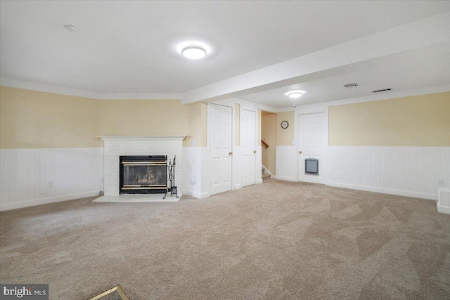 unfurnished living room featuring visible vents, a wainscoted wall, stairway, carpet flooring, and a brick fireplace