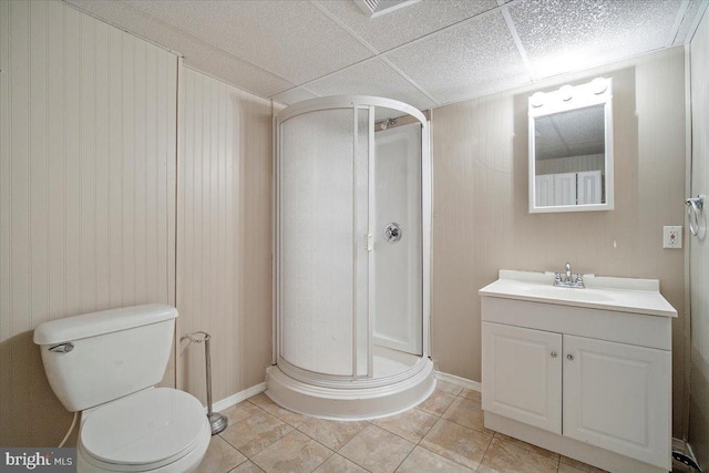 bathroom with toilet, a stall shower, vanity, a drop ceiling, and tile patterned floors