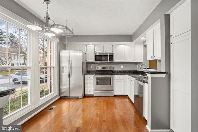 kitchen with white cabinets, dark countertops, light wood-style flooring, appliances with stainless steel finishes, and a sink