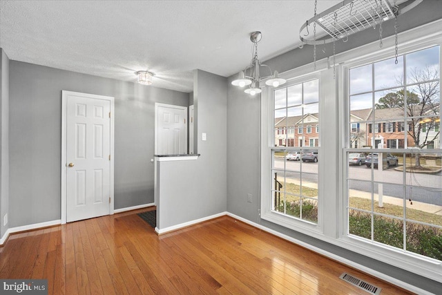 unfurnished dining area featuring visible vents, a textured ceiling, baseboards, and hardwood / wood-style flooring