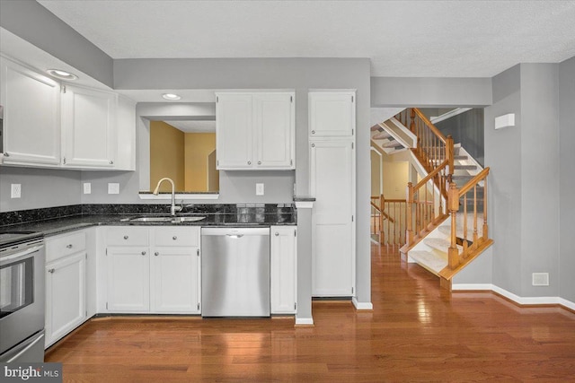 kitchen with stainless steel appliances, dark wood-style flooring, a sink, white cabinets, and baseboards