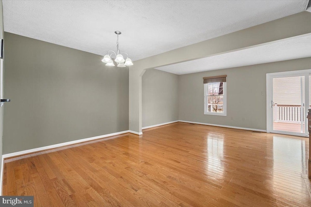 empty room featuring a chandelier, light wood-type flooring, a textured ceiling, and baseboards