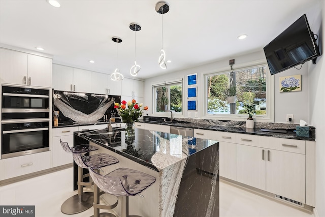 kitchen with hanging light fixtures, stainless steel appliances, a center island, white cabinets, and dark stone counters