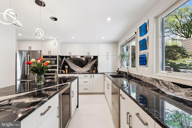 kitchen with sink, dark stone counters, pendant lighting, stainless steel appliances, and white cabinets