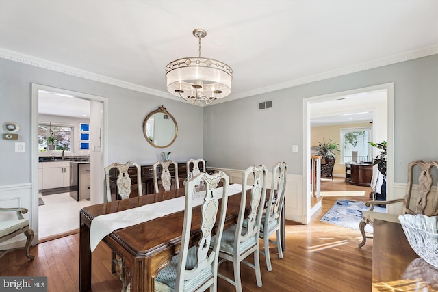 dining area with hardwood / wood-style flooring, crown molding, and an inviting chandelier