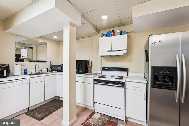 kitchen featuring sink, white cabinets, light tile patterned floors, a drop ceiling, and white appliances