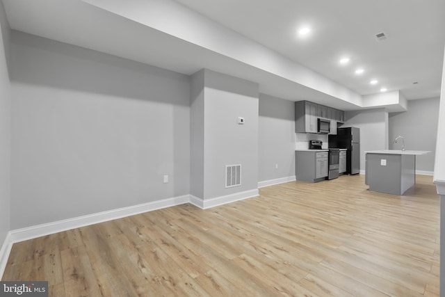 interior space featuring gray cabinetry, a kitchen breakfast bar, fridge, light hardwood / wood-style floors, and electric stove