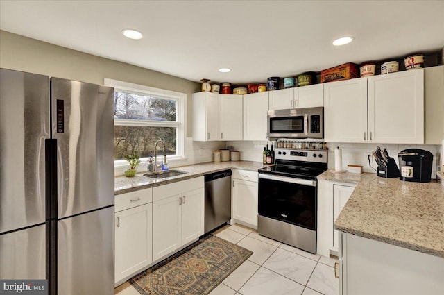 kitchen with sink, white cabinets, backsplash, stainless steel appliances, and light stone countertops