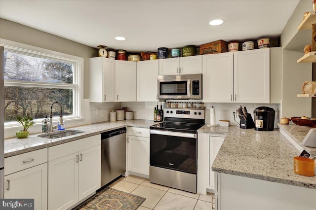 kitchen featuring sink, white cabinetry, light stone counters, appliances with stainless steel finishes, and backsplash