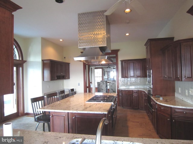 kitchen with a breakfast bar area, stainless steel appliances, light stone counters, island range hood, and a kitchen island