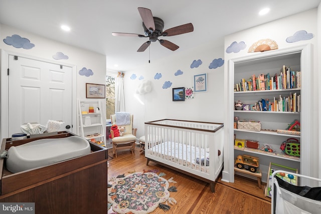 bedroom featuring a nursery area, ceiling fan, and hardwood / wood-style floors