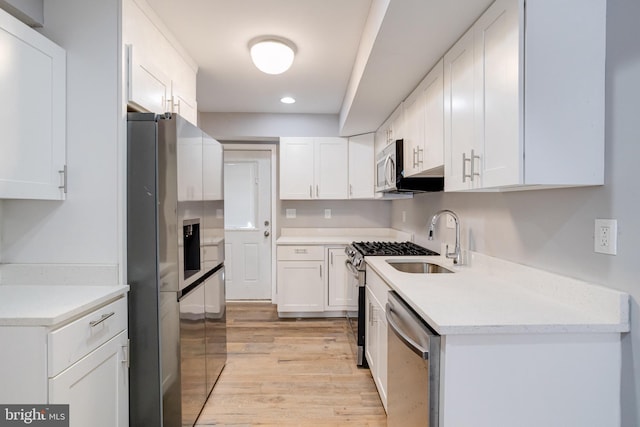 kitchen with appliances with stainless steel finishes, sink, white cabinets, and light wood-type flooring