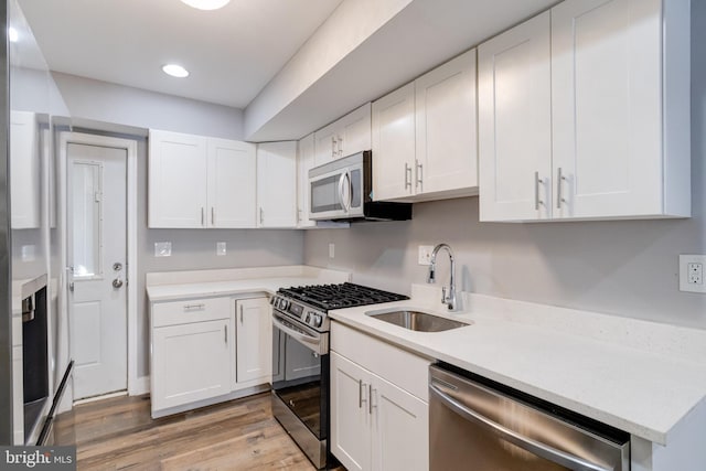 kitchen with white cabinetry, stainless steel appliances, sink, and light hardwood / wood-style flooring