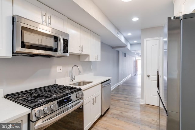 kitchen with appliances with stainless steel finishes, light hardwood / wood-style floors, sink, and white cabinets