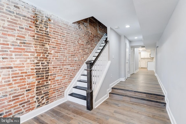 staircase featuring wood-type flooring and brick wall