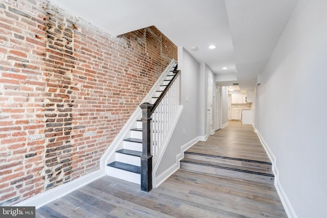 stairway with wood-type flooring and brick wall