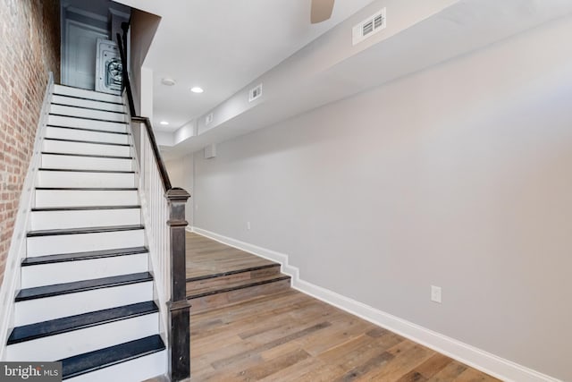 stairway featuring hardwood / wood-style flooring and brick wall