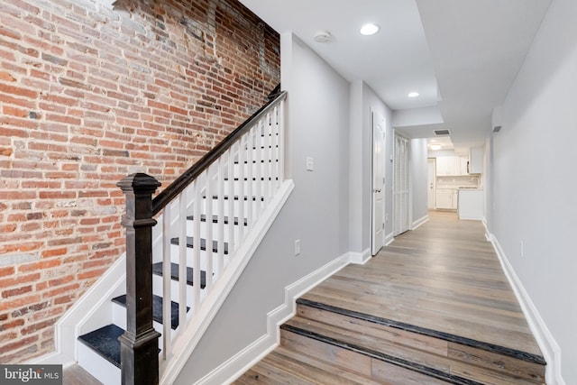 stairway with wood-type flooring and brick wall