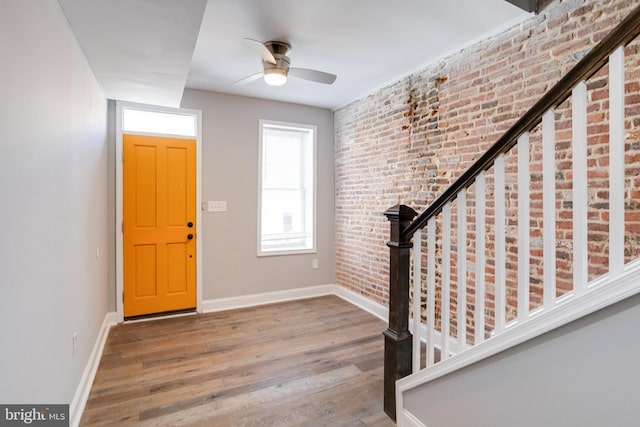 entryway featuring hardwood / wood-style flooring, ceiling fan, and brick wall