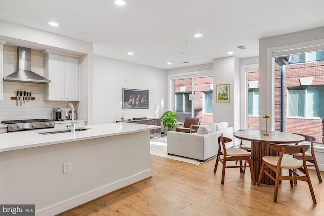 kitchen featuring wall chimney exhaust hood, sink, light hardwood / wood-style flooring, decorative backsplash, and white cabinets