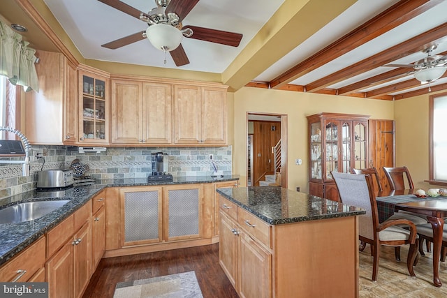 kitchen featuring ceiling fan, dark stone countertops, beam ceiling, a center island, and decorative backsplash