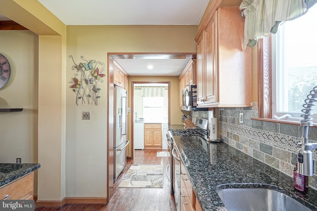 kitchen with light brown cabinets, light wood-type flooring, appliances with stainless steel finishes, dark stone counters, and decorative backsplash