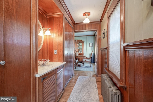 corridor featuring wood walls, ornamental molding, radiator, and light wood-type flooring