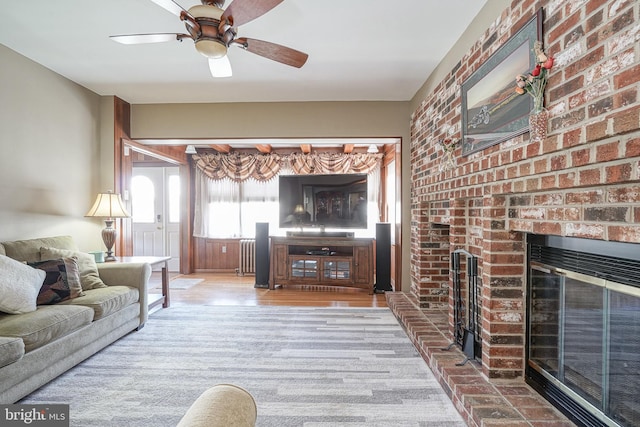 living room featuring ceiling fan, radiator, and a brick fireplace