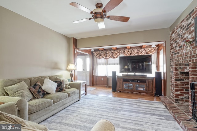 living room featuring ceiling fan, radiator heating unit, a brick fireplace, and light wood-type flooring