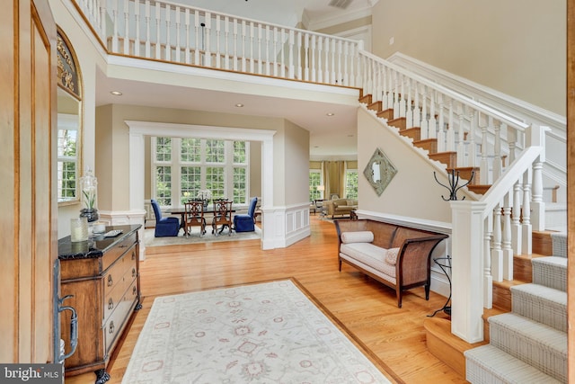 entryway featuring light wood-style flooring, a decorative wall, a towering ceiling, stairs, and wainscoting