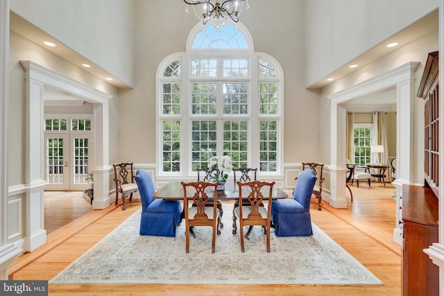 dining area featuring a chandelier, a decorative wall, a wainscoted wall, wood finished floors, and french doors