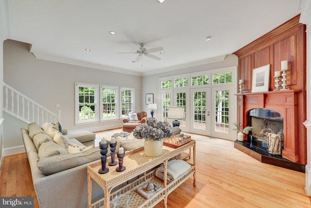 living area featuring a high end fireplace, light wood-type flooring, crown molding, and stairway