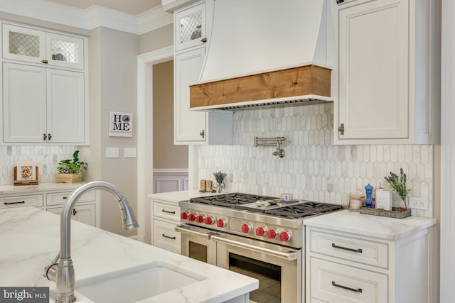 kitchen with premium range hood, white cabinets, ornamental molding, backsplash, and double oven range