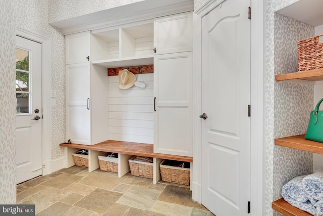 mudroom featuring baseboards, stone tile floors, and wallpapered walls