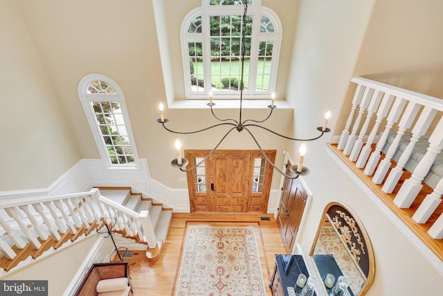 entryway with a decorative wall, wood finished floors, a towering ceiling, stairs, and wainscoting