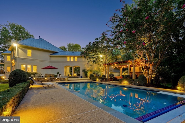 pool at dusk with a patio area, an outdoor pool, and a diving board