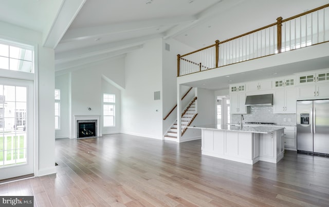 kitchen with white cabinetry, a kitchen island with sink, wall chimney exhaust hood, built in fridge, and beamed ceiling