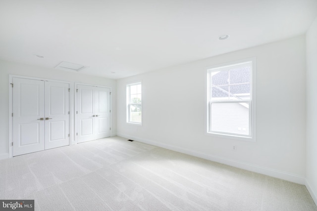 unfurnished bedroom featuring light carpet and two closets